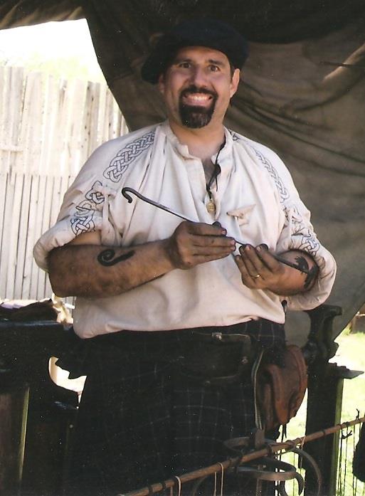 Michael in Celtic festival garb at the Celtic Dragon Blacksmith Shoppe, holding a hand-forged S-hook.