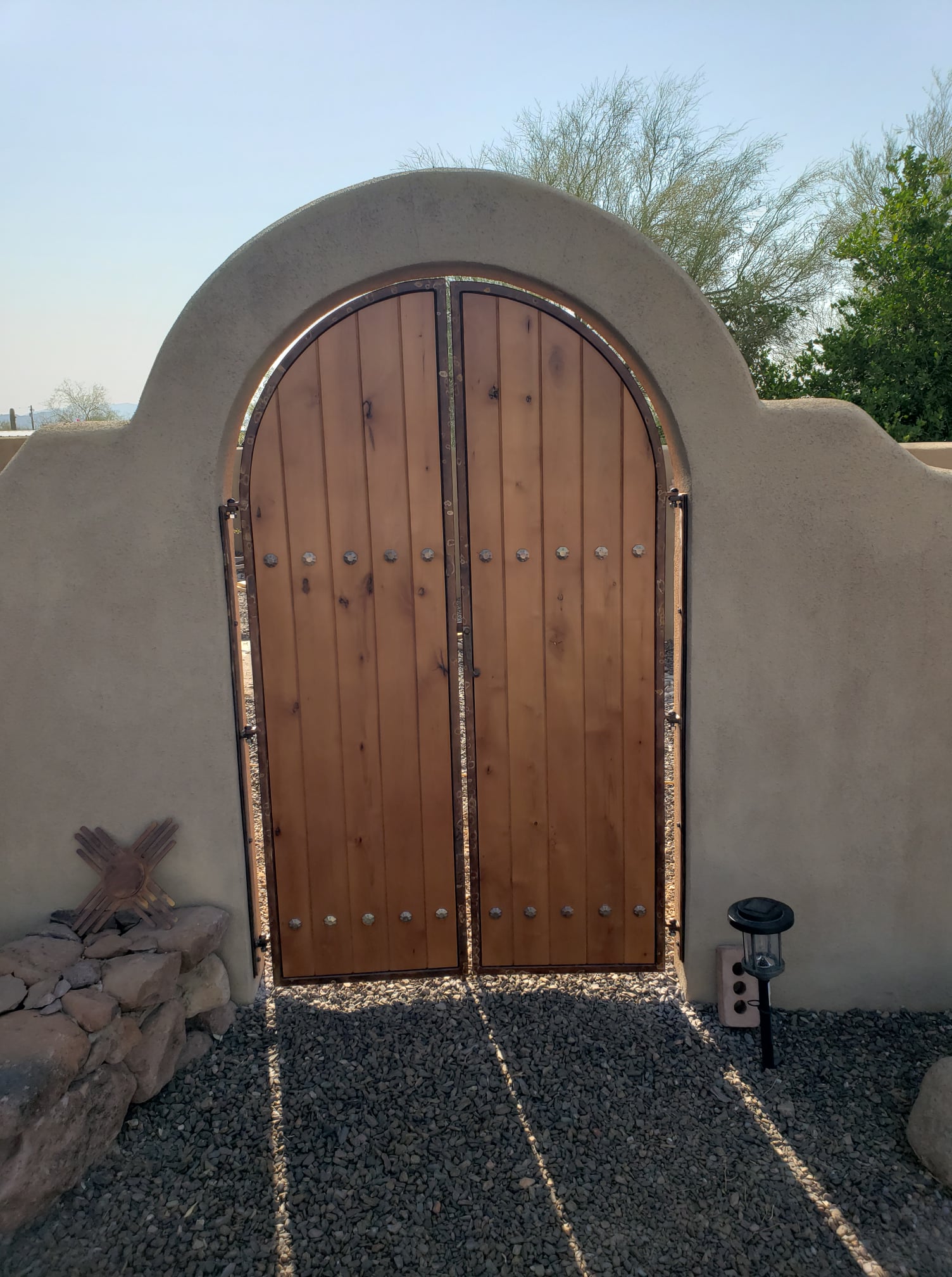Custom arched wood and iron gate set into an adobe wall.