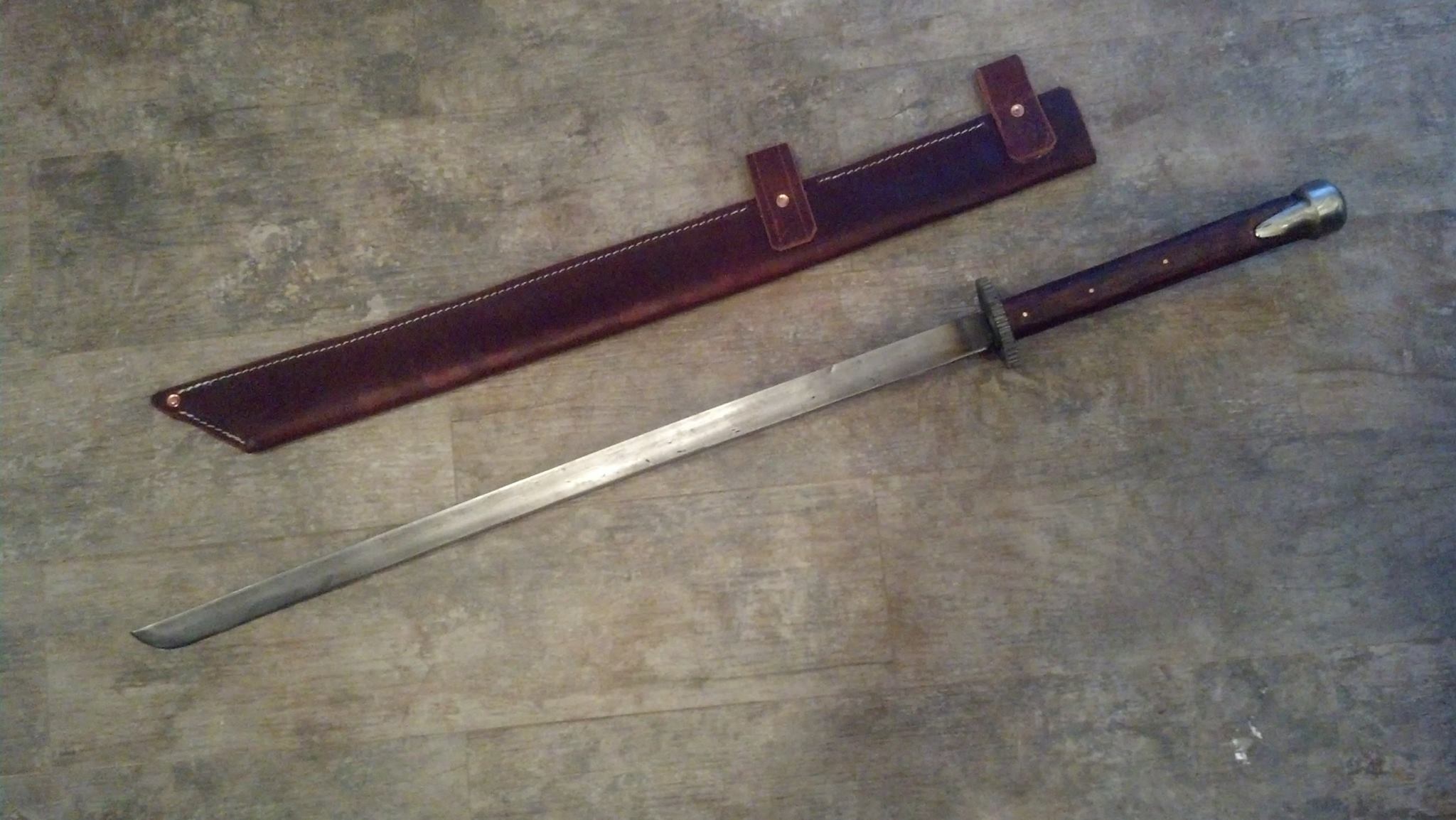 Forged sword laid alongside a custom leather scabbard.