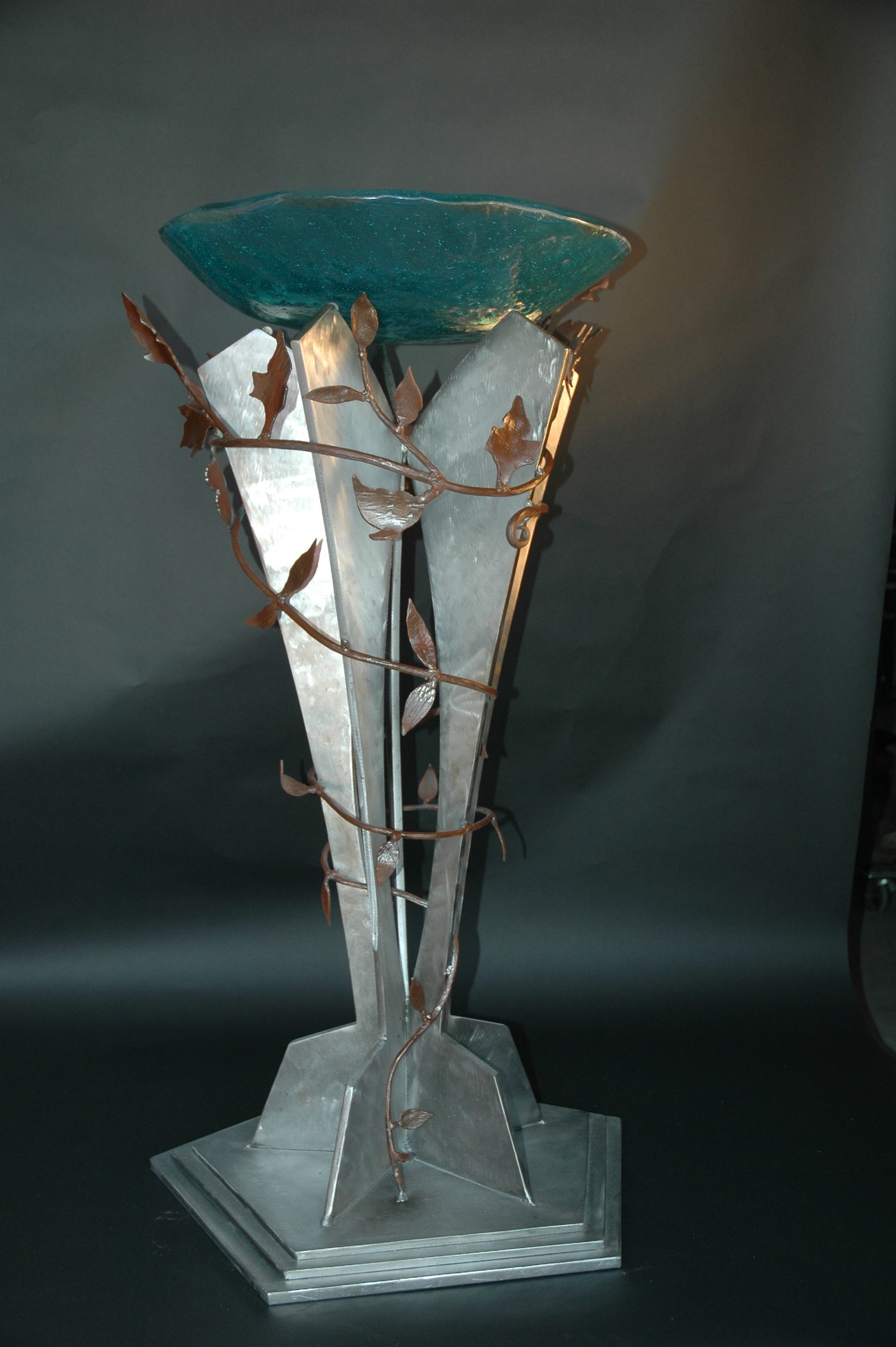 Forged steel metal artwork with copper vines wrapping the base and a hand-blown blue glass bowl.